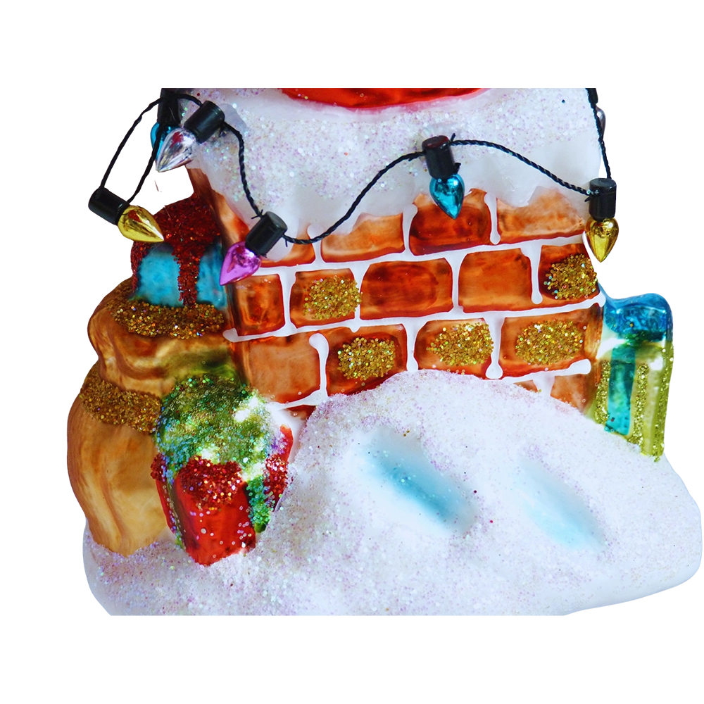 Dettaglio della base del camino: mattoni arancioni con glitter oro, lucine colorate, sacco di regali, pacchetti rossi, verdi e azzurri e neve glitterata con impronte azzurre