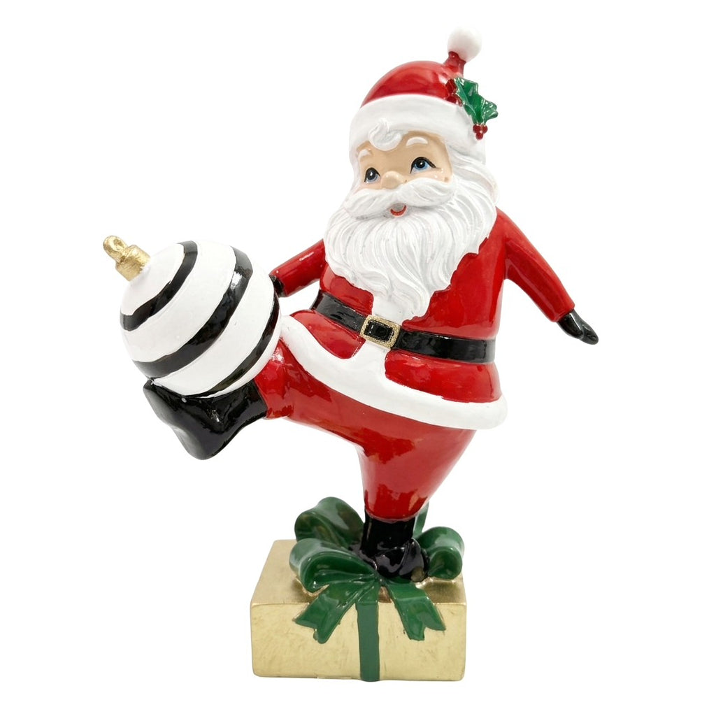 Decorazione natalizia in poliresina, Babbo Natale che calcia una palla di Natale a righe bianche e nere su un pacco regalo dorato