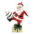 Decorazione natalizia in poliresina, Babbo Natale che calcia una palla di Natale a righe bianche e nere su un pacco regalo dorato