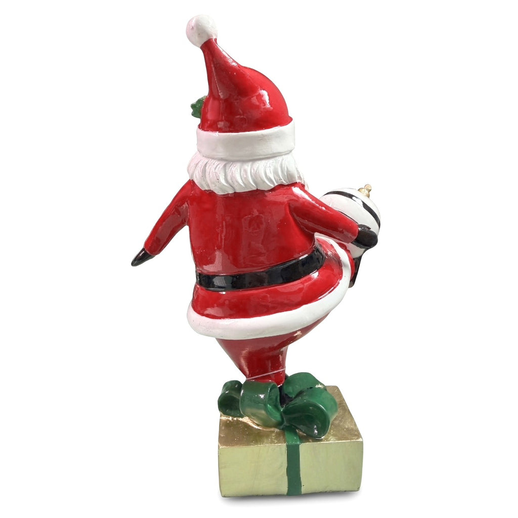 Babbo Natale in poliresina visto da dietro in equilibrio su una gamba sul pacco regalo dorato con fiocco verde, con cappello rosso
