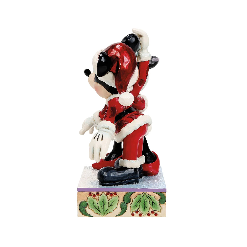 Vista laterale: Topolino in profilo con cappello rosso da Babbo Natale e orecchie a scacchi blu, con Minnie dietro di lui che alza il braccio con il vischio