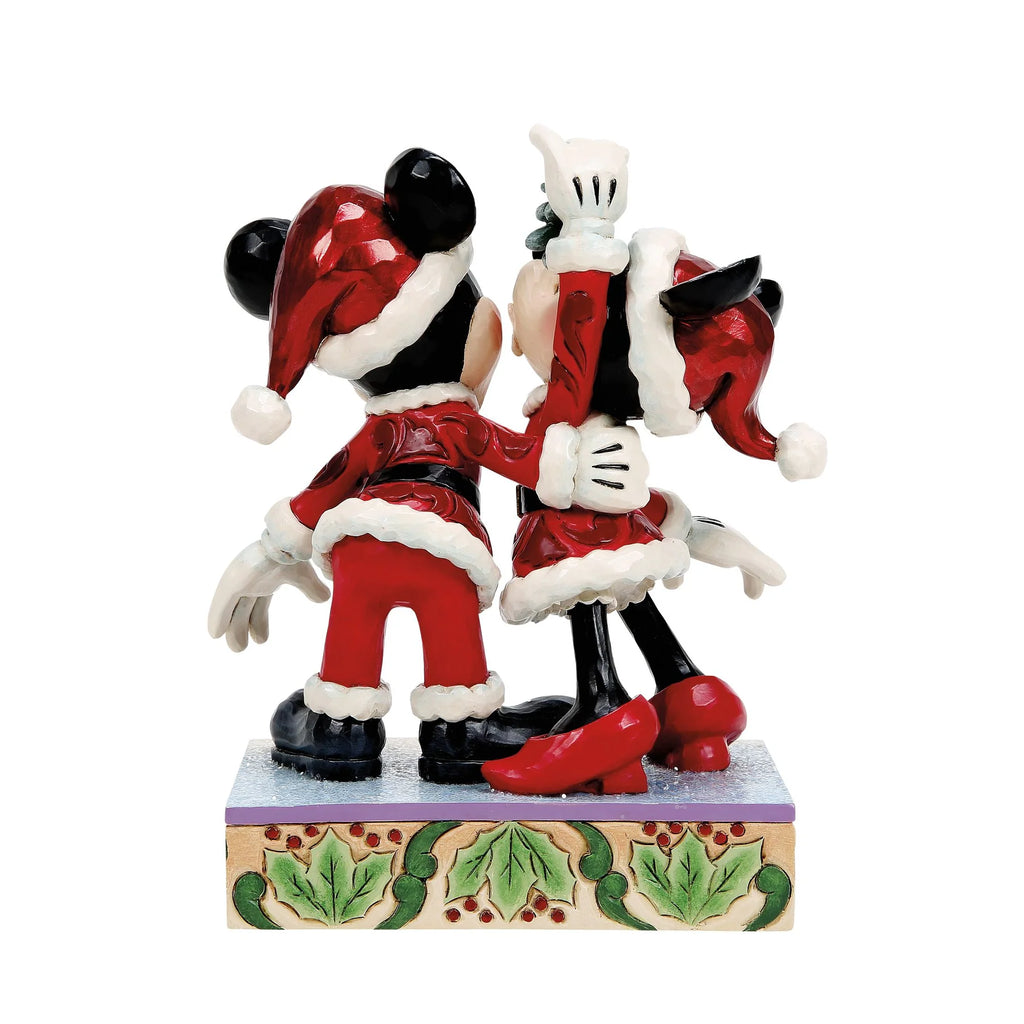 Topolino e Minnie visti da dietro con cappelli rossi con pompon bianco e giacche bordate di bianco, mano di Minni alzata con il vischio, base con agrifoglio
