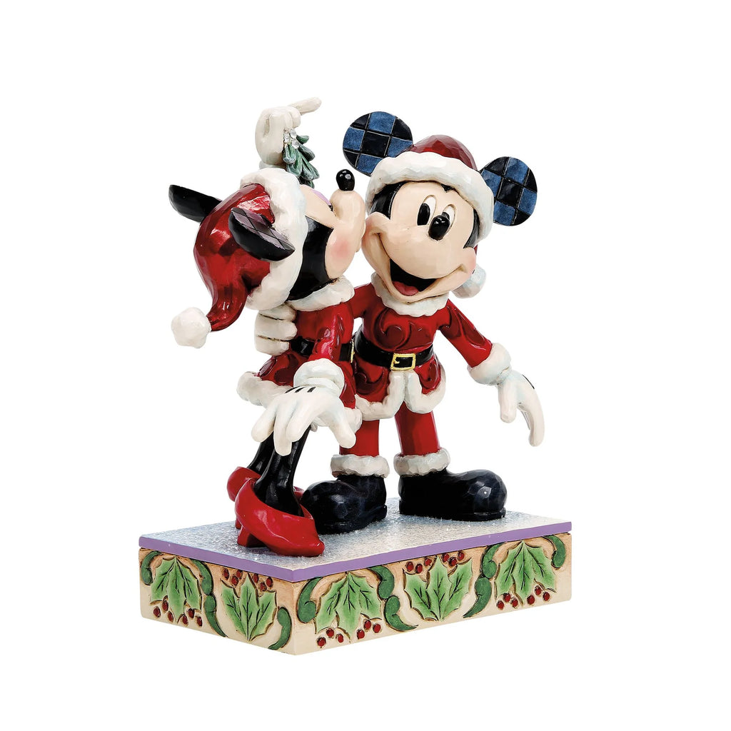 Topolino e Minnie visti di tre quarti dal davanti: Minnie bacia Topolino sotto il vischio, con cappelli rossi, orecchie a scacchi e base con agrifoglio e bacche rosse