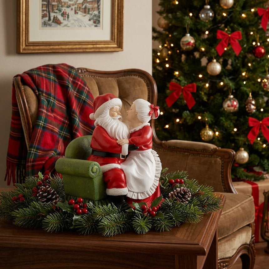 Statuina di Babbo Natale e Mamma Natale che si abbracciano seduti su una poltrona verde, appoggiata su un tavolino di legno con rametti di abete, pigne e bacche rosse davanti a un albero di Natale illuminato