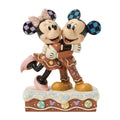 Statuina di Topolino e Minnie abbracciati, vestiti da biscotti di pan di zenzero, con orecchie a scacchi blu e lilla e fiocco rosa a righe, su base di glassa bianca con caramelle pastello