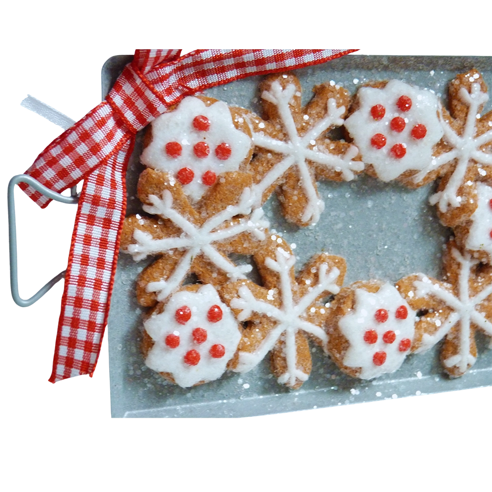 Dettaglio della teglia con biscotti di pan di zenzero a forma di fiocco di neve, alcuni glassati di bianco con puntini rossi, e fiocco a quadretti rossi e bianchi